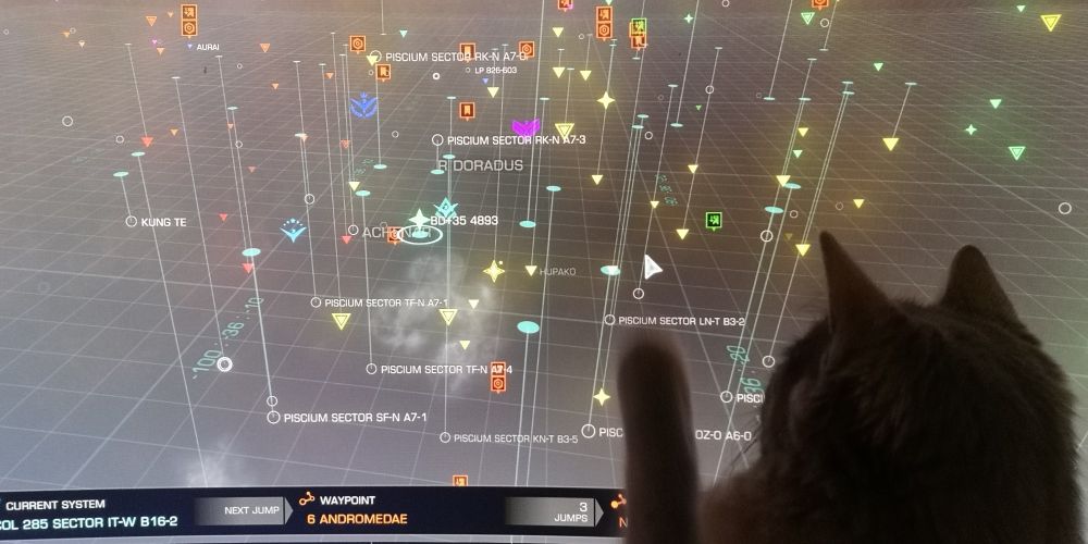 A photo of a kitten taking a swipe with her paw at the mouse cursor on the galaxy map screen in Elite Dangerous. 