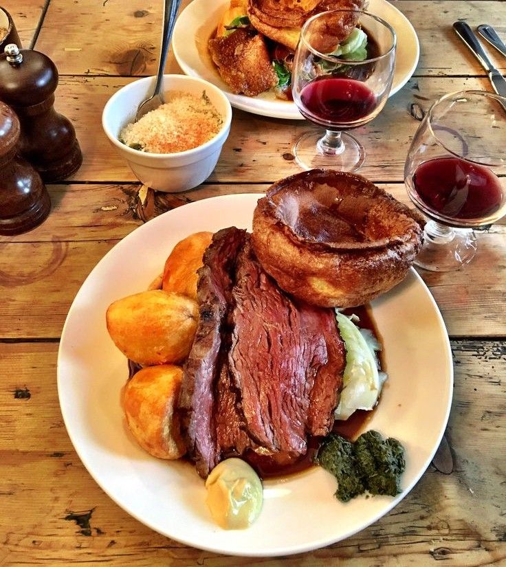 Sunday roast dinner with beef, roast potatoes, Yorkshire pudding, greens, and red wine.