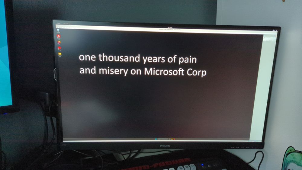 a computer booting a windows 11 VM, the background says "one thousand years of pain and misery on Microsoft Corp"