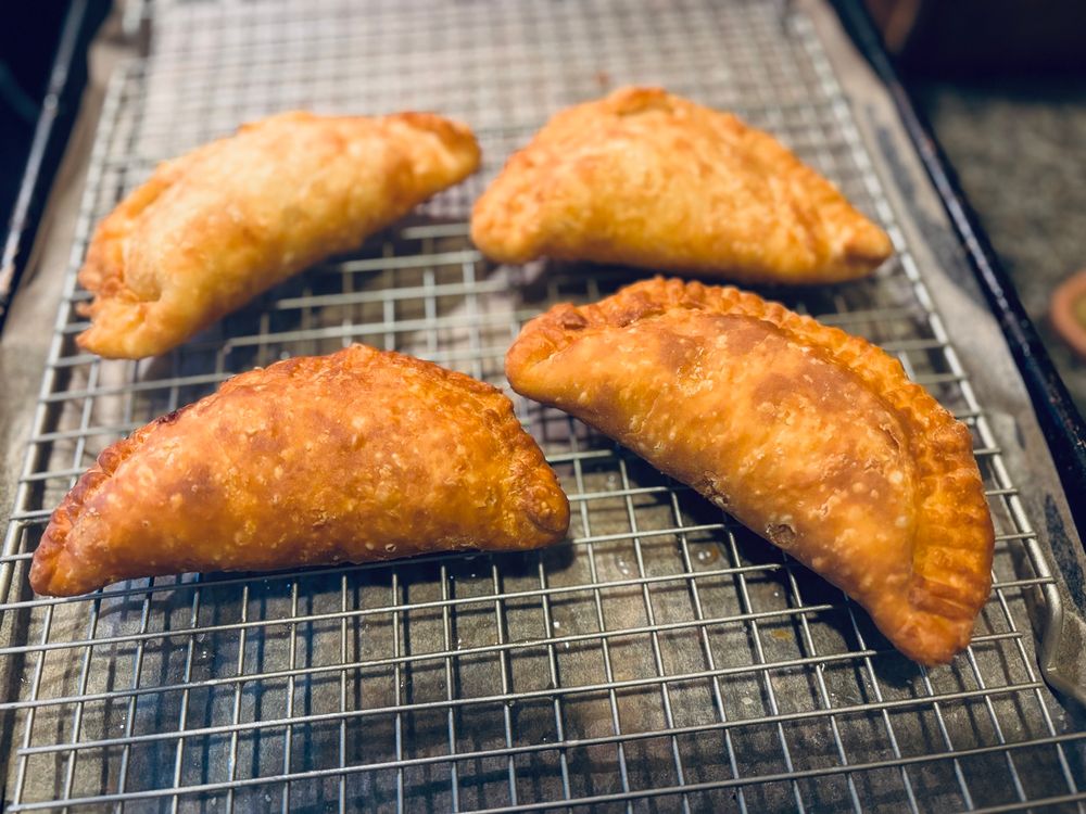 Four golden brown peach pies (half moon shaped) cooling on a wire rack