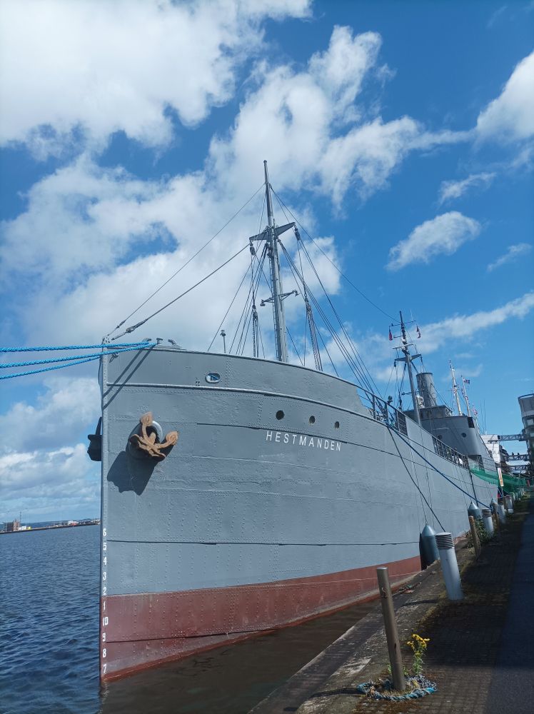 A grey ship with a red stripe and rusty anchors, docked at Leith