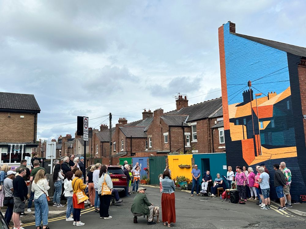 A fair crowd of people watching Mariners and Marras singing in front of the new mural on the corner of Linskill Terr and Lindisfarne Terr, North Shields 