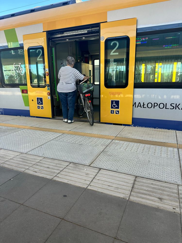 An older woman pushing a bike on to a Polish regional train. 