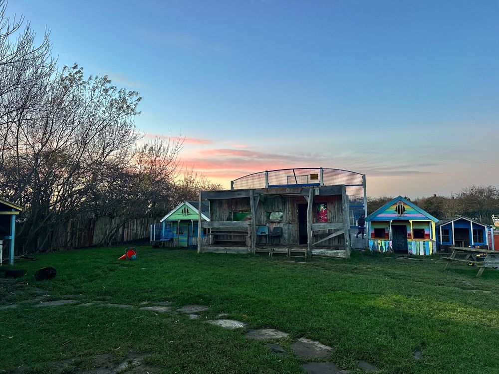 The sun setting behind some wooden playhouses and a caravan at Shiremoor Adventure Playground 