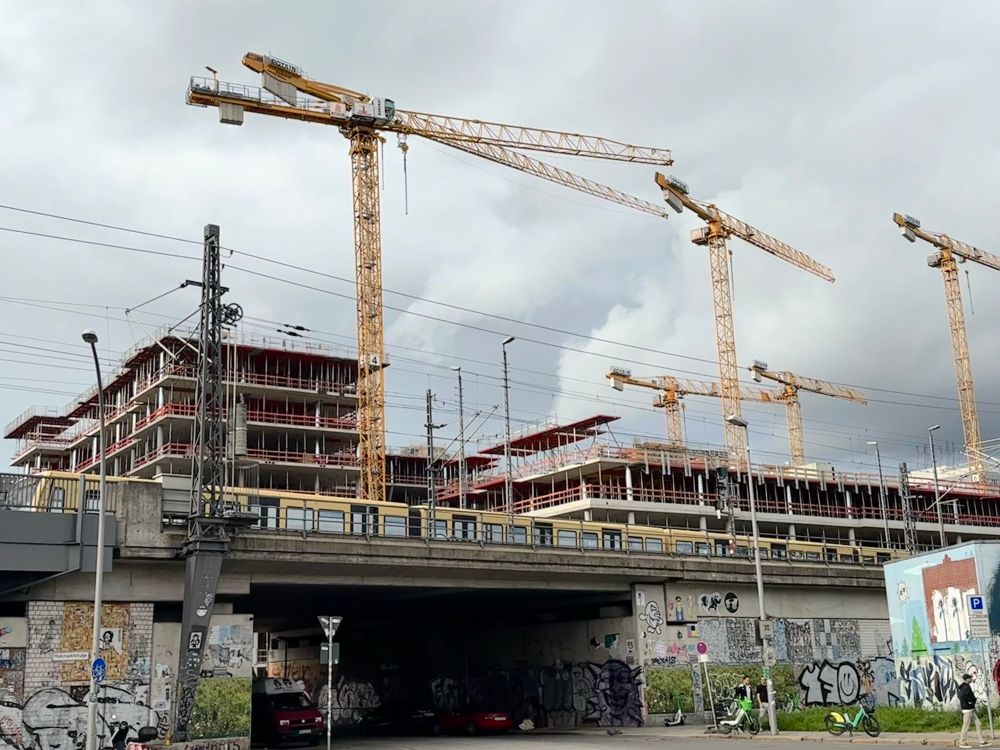 A s-bahn passing across a bridge with a building site and cranes in the background. 