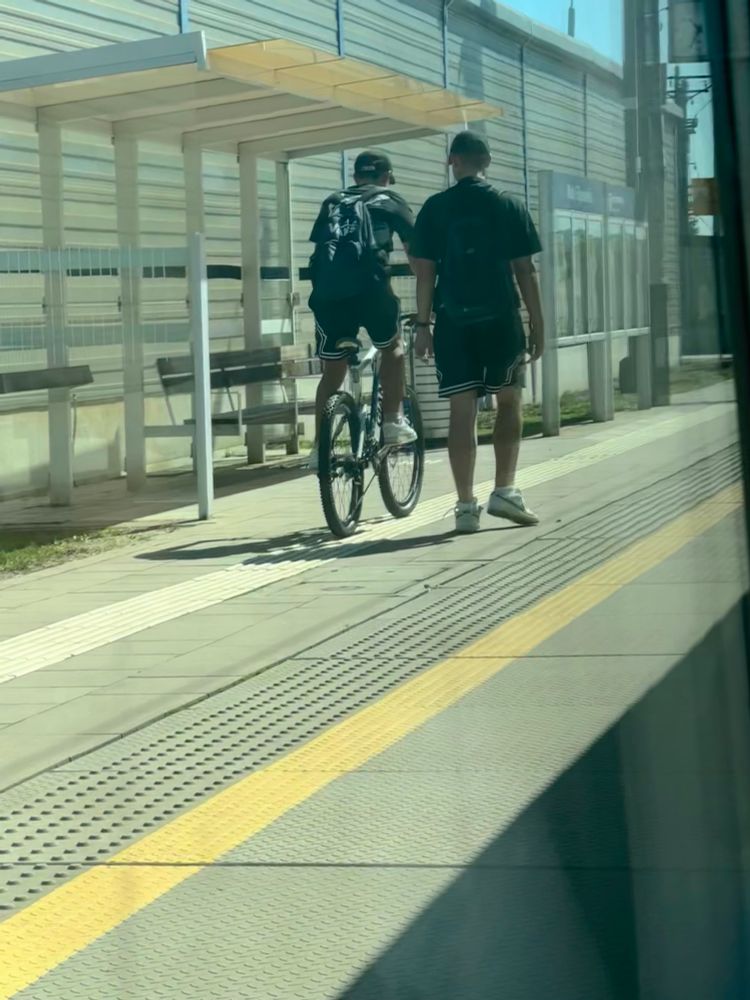 A teenage boy cycling a bike away from a train at a suburban Polish station 
