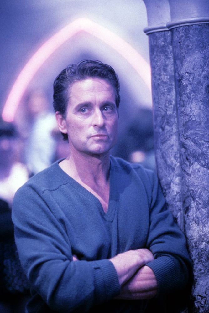 Michael Douglas in a plain-knit deep V-neck jumper, neon night club lights behind him.