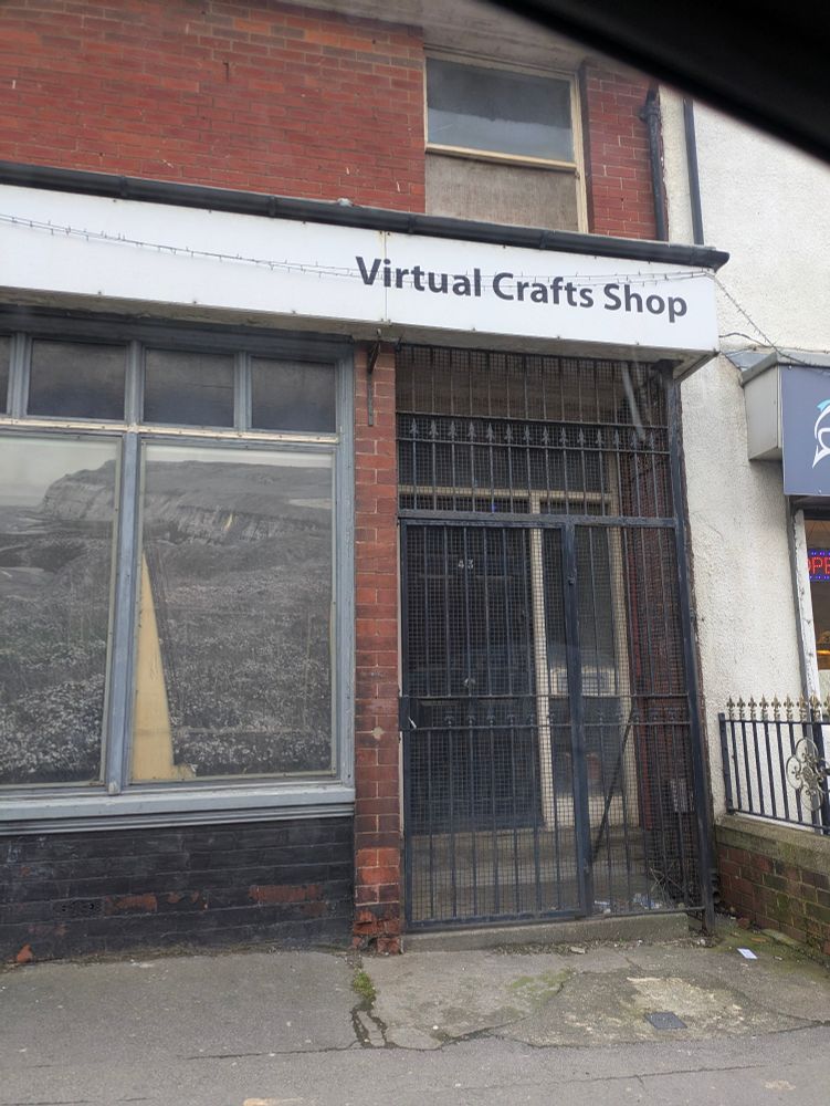 Shabby, closed-down shop with black metal gate over the entrance way. Name of shop is 'Virtual Crafts Shop'