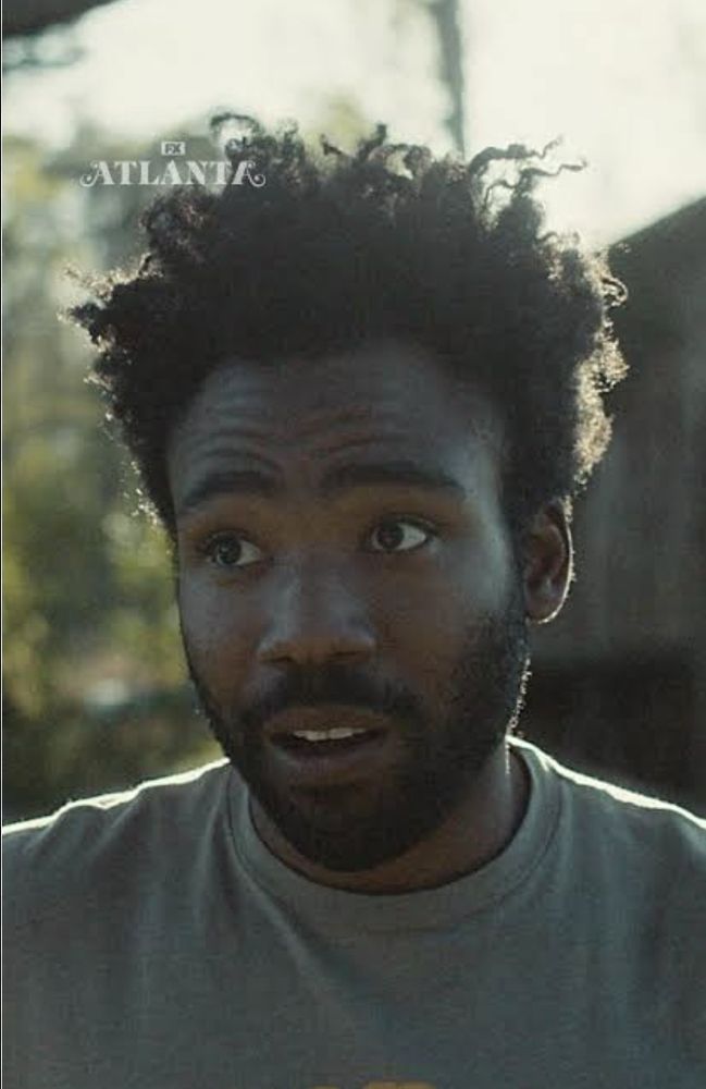 Rosto de Earn, personagem de Atlanta interpretado por Donald Glover, homem negro de barba e cabelo cacheado, nem curto, nem comprido, camisa que me parece cinza. No fundo, vemos o verde de árvores e um pedaço de um celeiro, ambos desfocados. Ele está de olhos arregalados, arqueando as sobrancelhas e franzindo a testa, parecendo preocupado, e com a boca entreaberta como quem vai falar. Cena da série em que ele explica a Darius que, por ser pobre, ele não pode investir dinheiro que vai render daqui há meses, pois suas necessidades são agora.