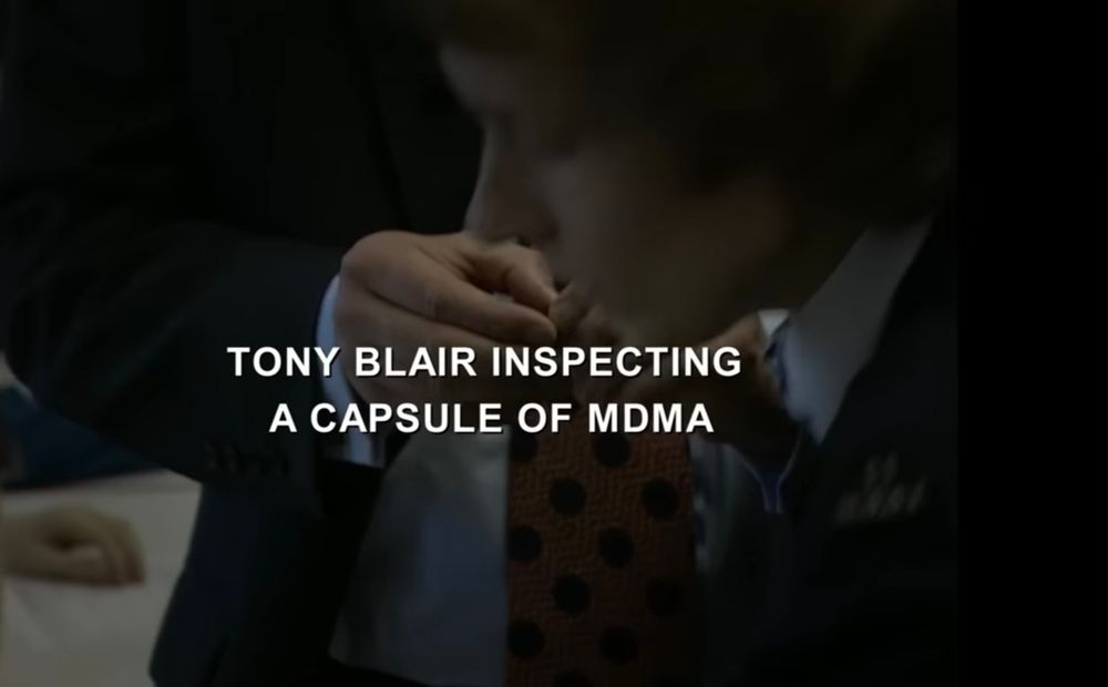 Imagem de um rosto de uma pessoa se levantando, e de mãos de alguém vestindo terno e gravata segurando algum objeto pequeno. A legenda diz "Tony Blair inspecting a capsule of MDMA"