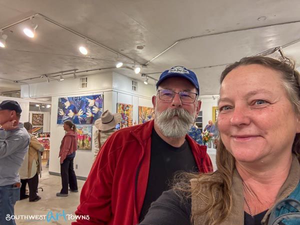 Man and woman taking an ussie with an art gallery exhibit in the background.