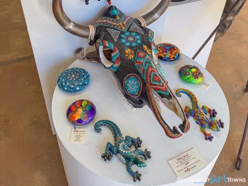 Various pieces of art decorated in a dot painting technique by Terri Durham including a skull, circular rocks, and geckos.