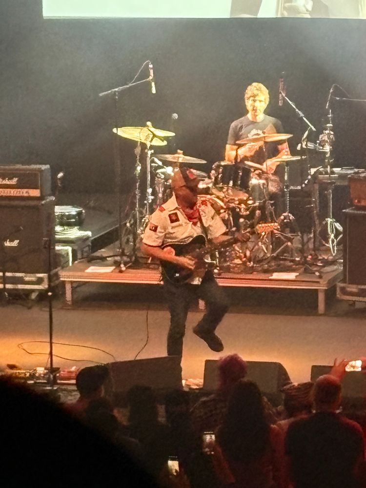 Tom Morello in a white shirt with a black guitar performing at Lincoln Theater. 