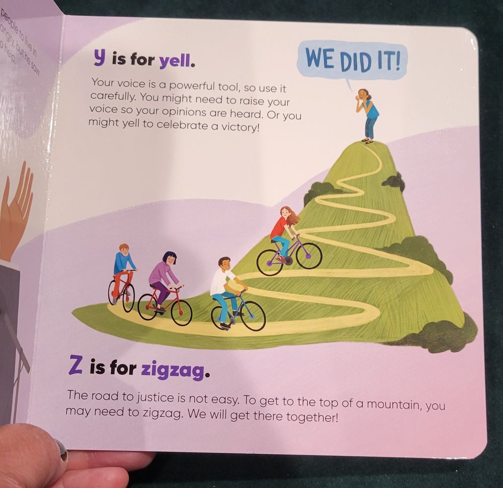 page from children's board book. Illustration of a mountain with people riding bicycles up switchbacks. One person at the top yells "WE DID IT!" 