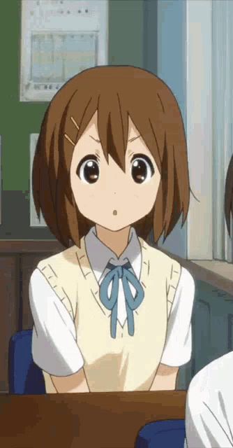 a girl with brown hair is sitting at a desk in a classroom and looking at the camera .