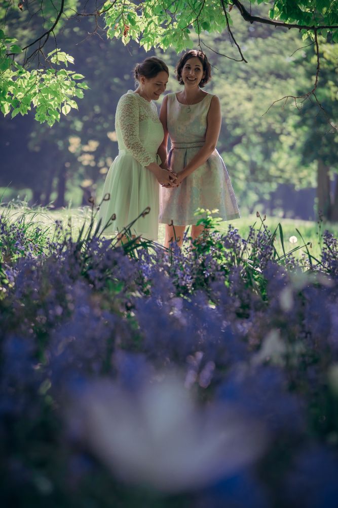 Brautpaar Lisanne und Anna steht in einem lila Blumenfeld im Park. Anna schaut lachend nach unten, Lisanne schaut in die Kamera.