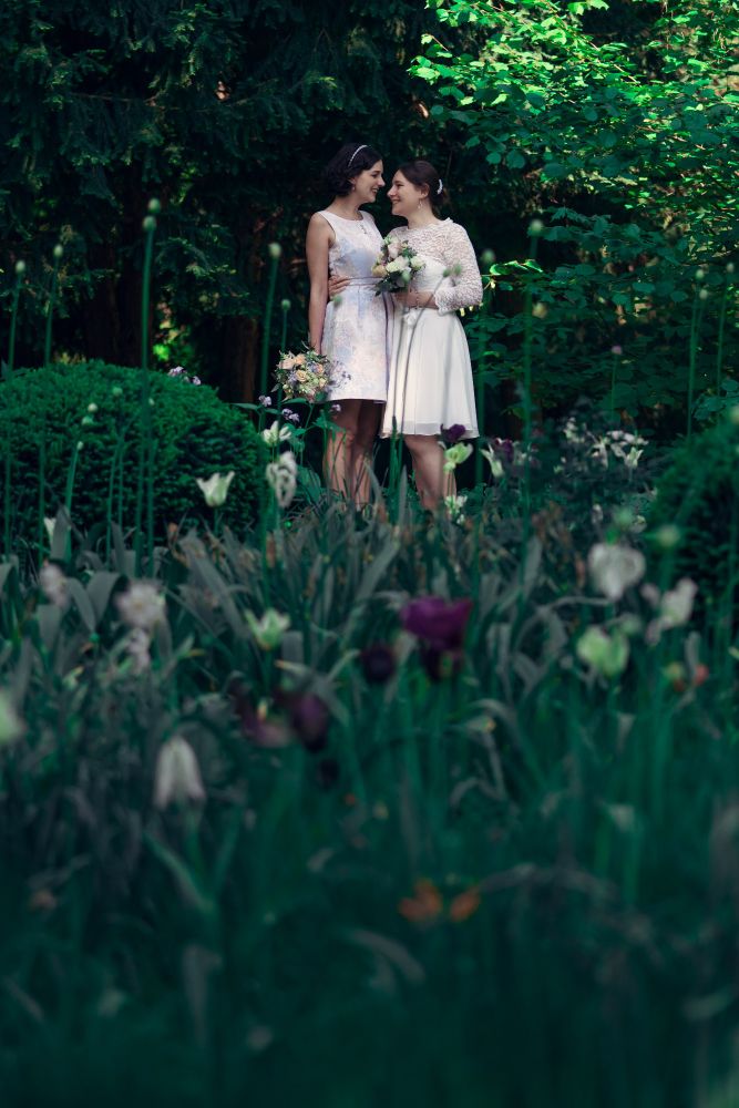 Brautpaar Lisanne und Anna steht in einem Blumenfeld im Park und die beiden sehen einander an.