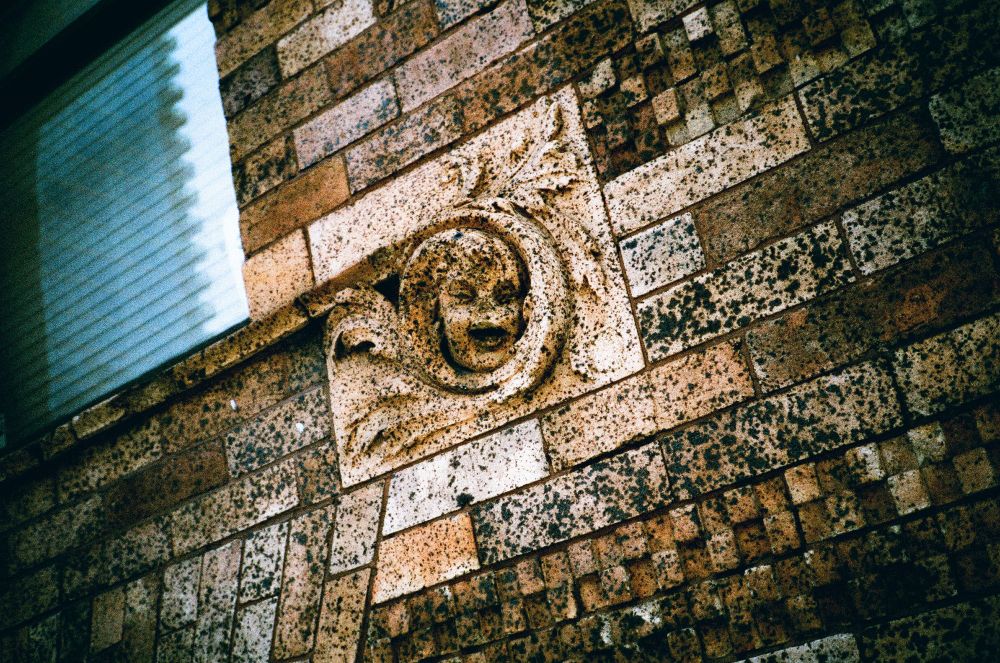 a small stone sculpture of a face with dark eyes and mouth inset among other bricks in the wall