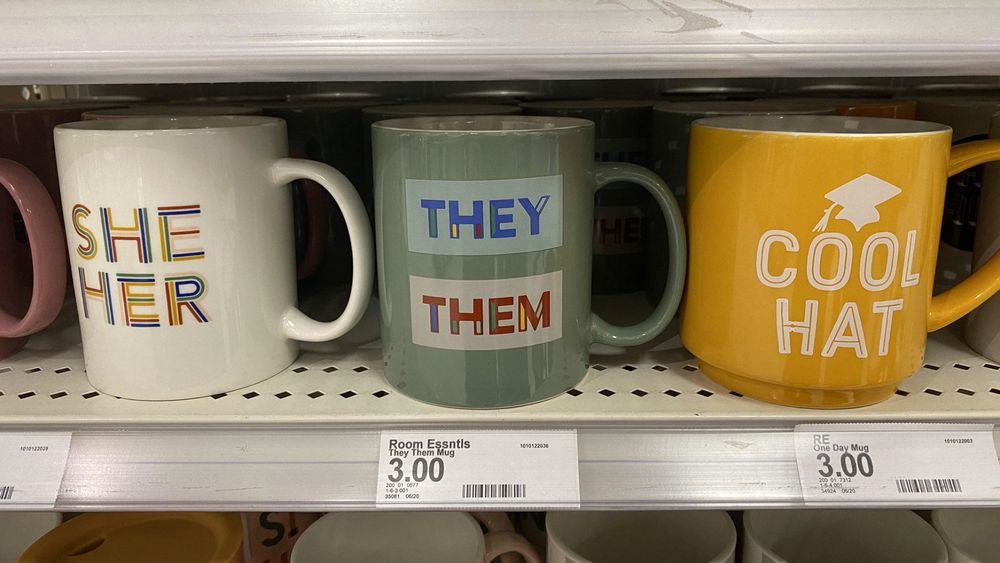 Mugs that from left to right say; She Her, They Them, and Cool Hat