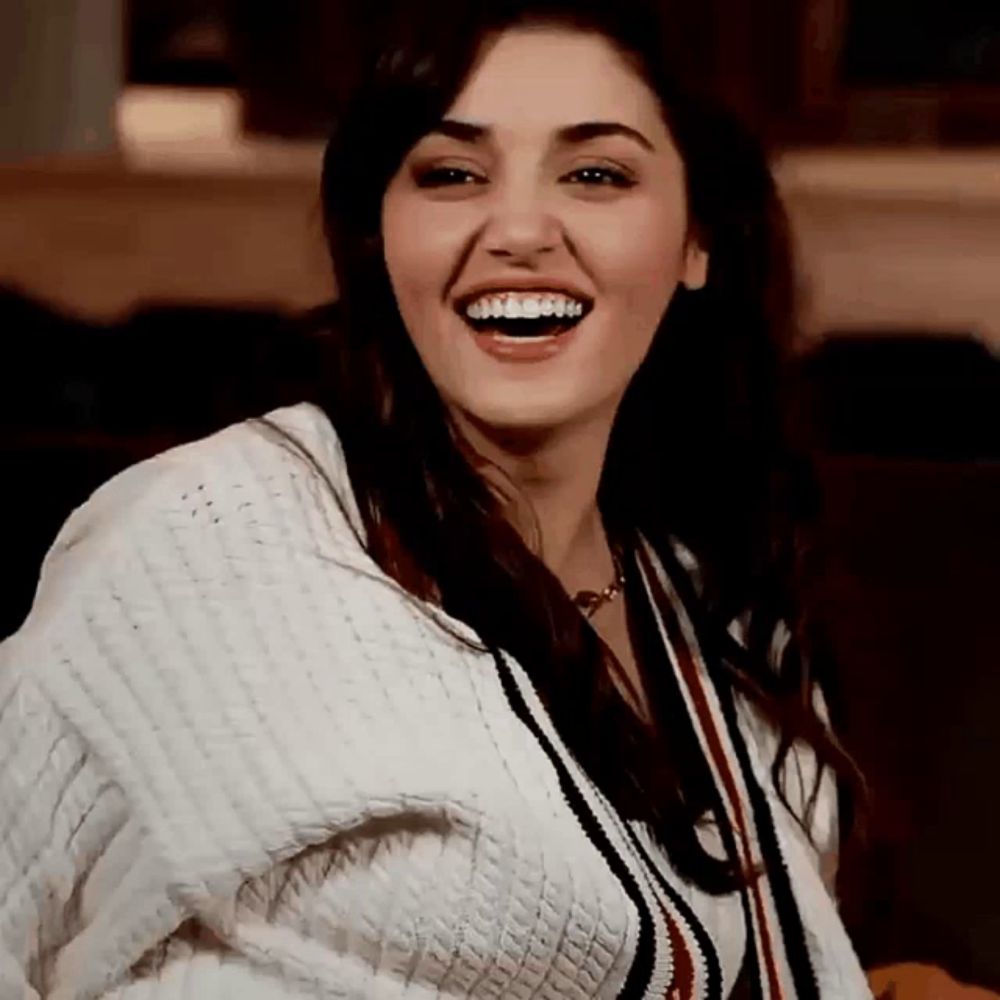 a woman wearing a white sweater is laughing with her mouth open