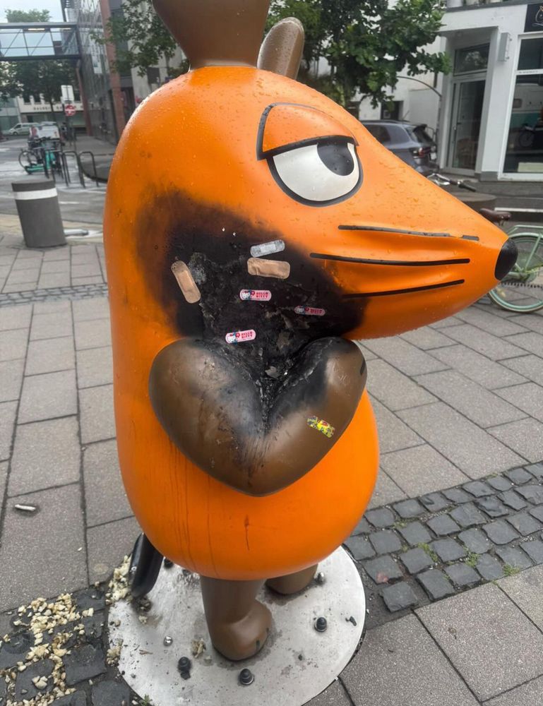 Die angekokelte Mausstatue, auf dem Brandfleck sind viele Pflaster.