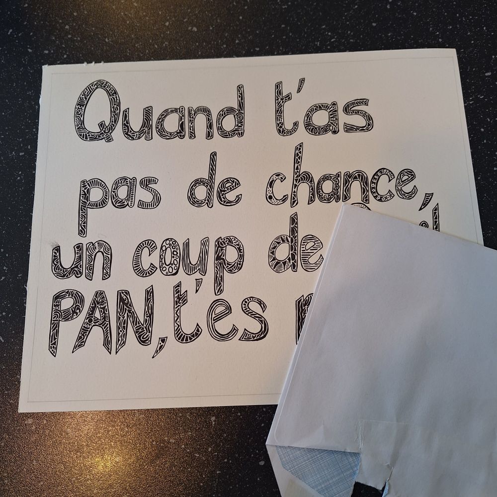 Feuille blanche posée sur un plan de travail noir moucheté.
Sur cette feuille, on peut lire "Quand t’as pas de chance, un coup de (***) PAN, t’es (***)".
Les lettres sont tracées en script dont l’intérieur est décoré de motifs noirs.