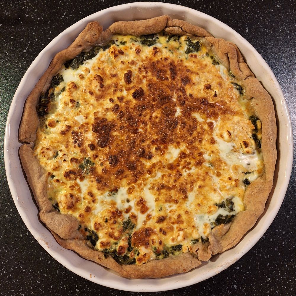 Tarte épinards et feta dans une tourtière en céramique blanche.