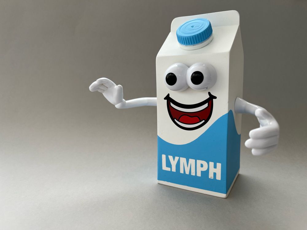 A milk-carton sized and shaped mascot character, complete with eyes and arms. The lower half of the milk carton body is emblazoned with a blue wave, with the front containing the word “Lymph” in large bold letters. The mascot is pictured against a smooth grey backdrop.