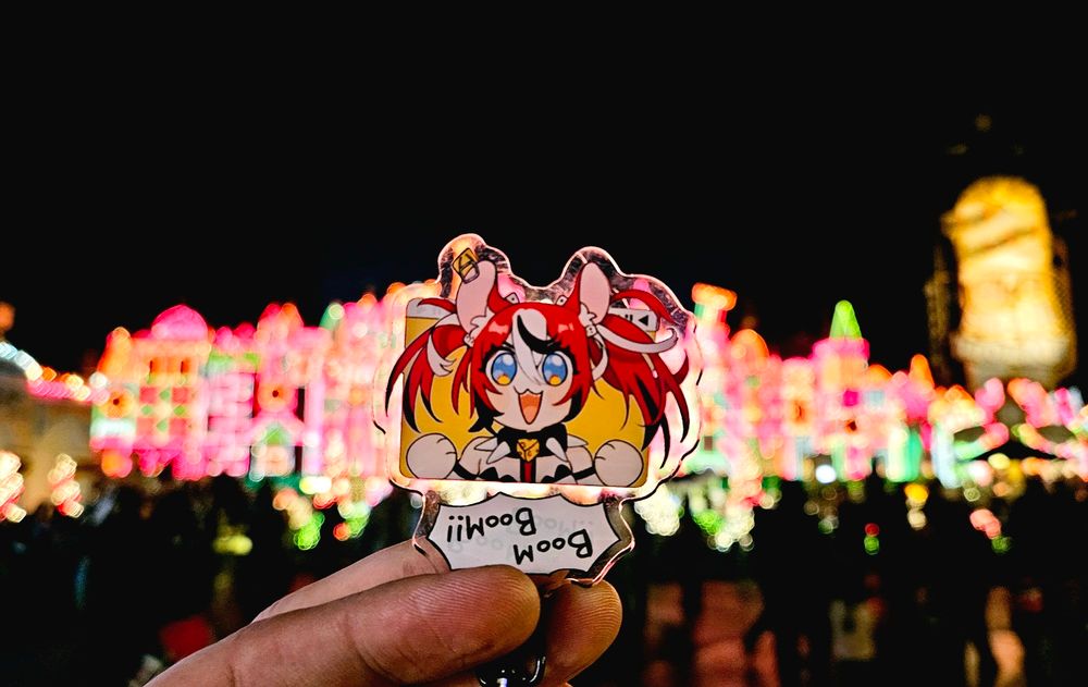 A keychain of Hakos Baelz in front of Christmas lights at Disney