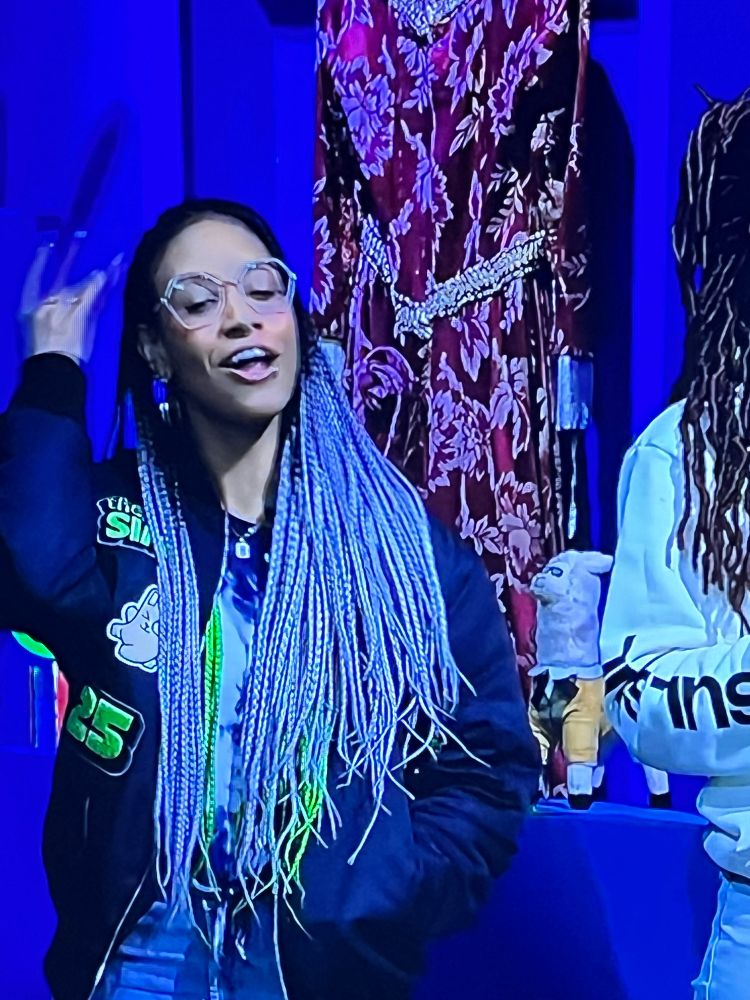 Snap of 25th Sims birthday hosts with a red and gold medieval style dress hung up in the background 