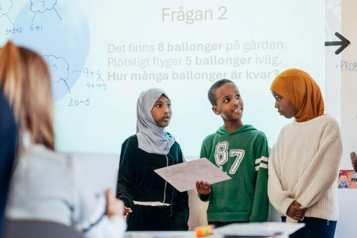 Tre elever står framför klassen och berättar om hur de löst en matematikuppgift ihop.