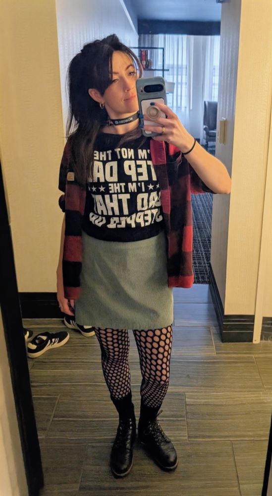 A mirror selfie of Sarah's PaxU Day 2 outfit. Black boots with tights, a grey skirt, a red and black flannel, and a shirt that says "I'm not the Stepdad, I'm the dad that stepped up."