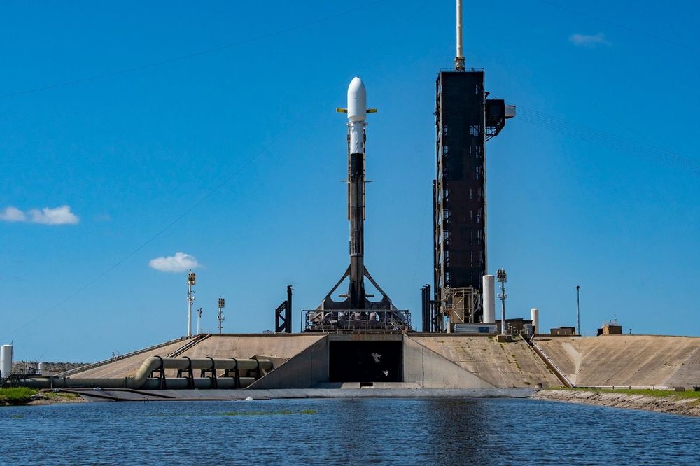 Rocket on launch pad. Blue skies in the background and water in the foreground.