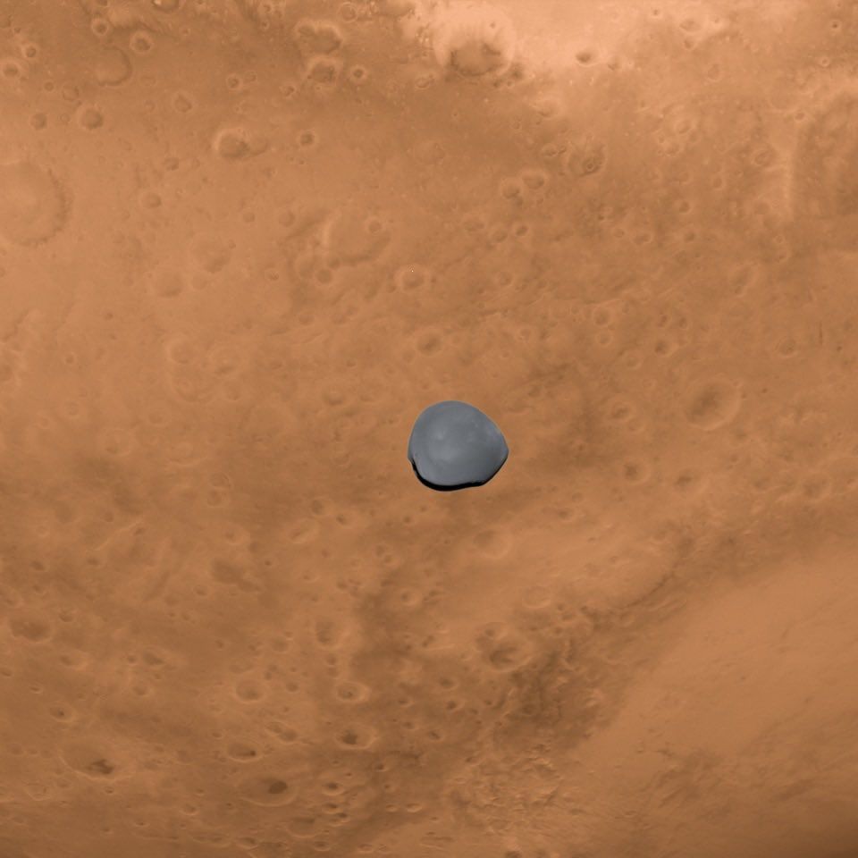 A false-colour Asteroid Framing Camera image of Deimos, showing what the moon would look like to an astronaut in orbit around Mars, seen a orange-red background. 