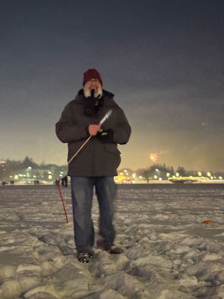 Bearded man standing on snow holding a small rocket. (Aka @samer.is on Tjörnin on NYE!)