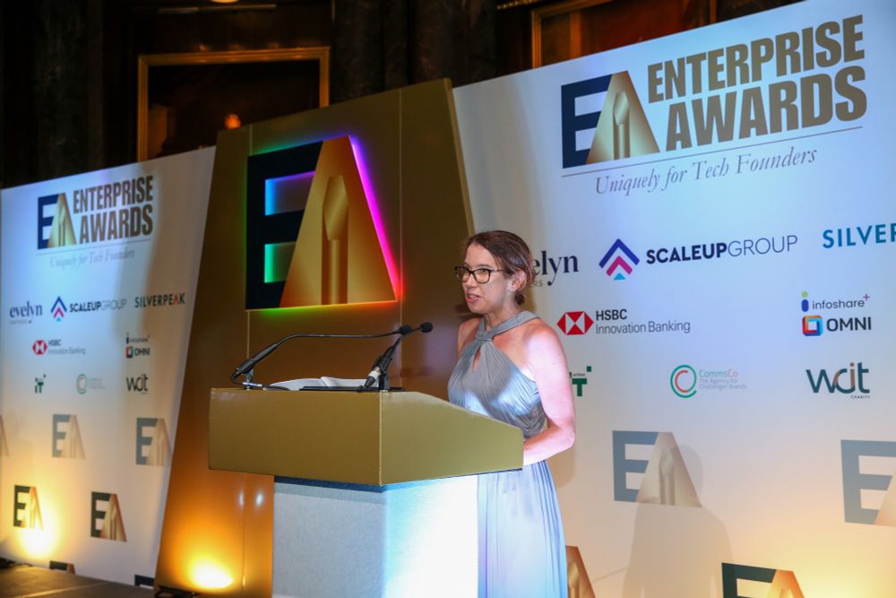 A lady in a silver dress standing at a lectern with the words Enterprise Awards on the screen behind her.