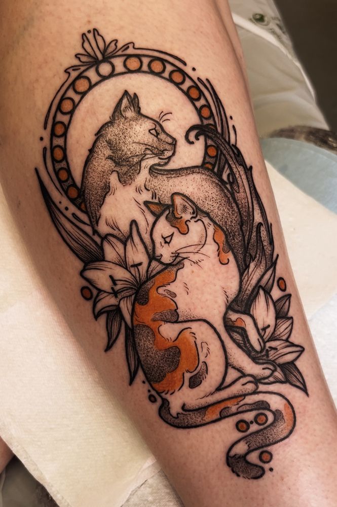 This is an image of a tattoo on a woman’s leg. The tattoo is of two cats and some stargazer lilies in art nouveau style. The tattoo is done in black line work with stipple shading and accents of orange. Done by Molly Vee in Seattle WA. 