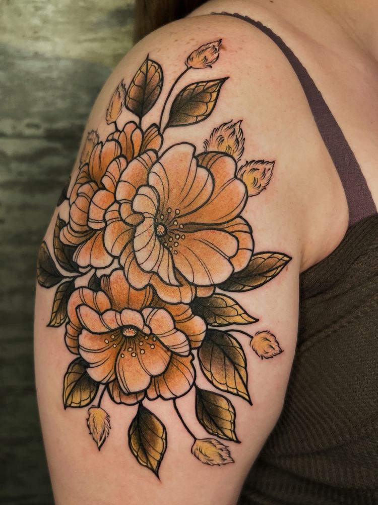 The image shows a woman’s upper arm with a fresh tattoo. The tattoo is of wild roses and bunny tail grass. The tattoo is all done in shades of brown and gold with strong black outlines. The tattoo is done in Neotraditional style in sepia tone.