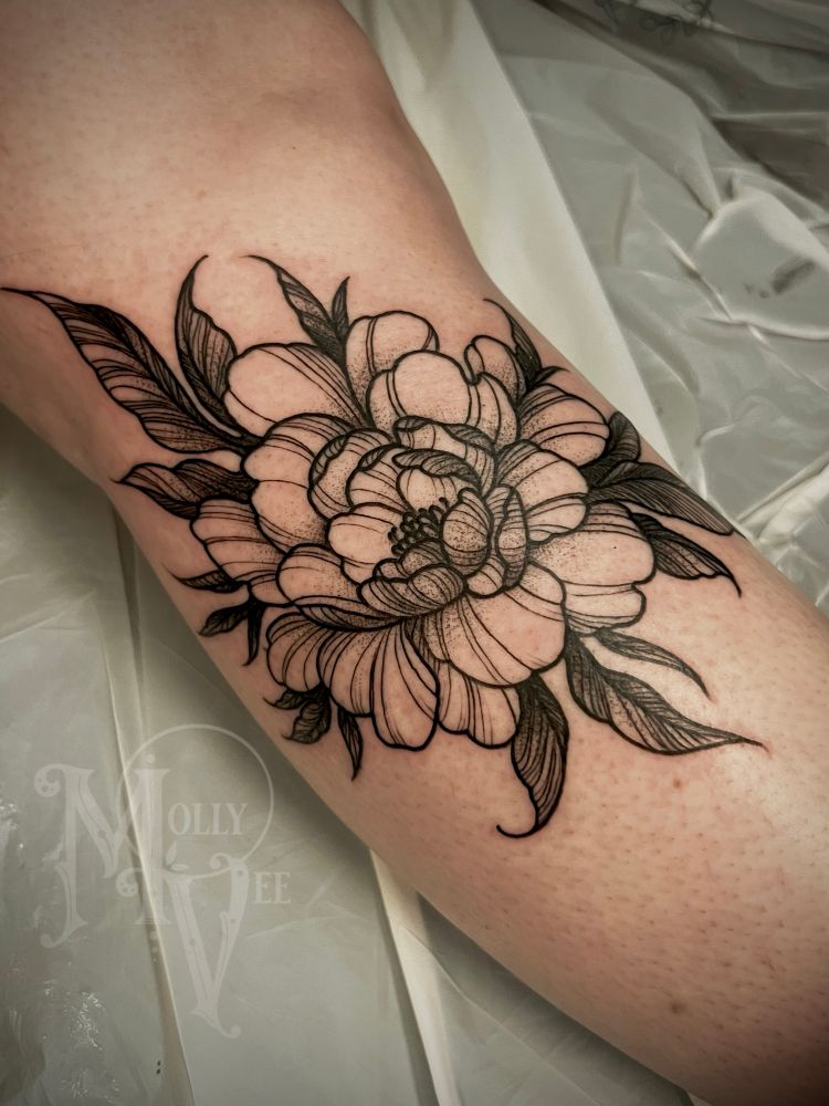 This is a photo of a woman’s lower leg with a fresh tattoo of a peony done in black line work style with dot work and fine line details. 