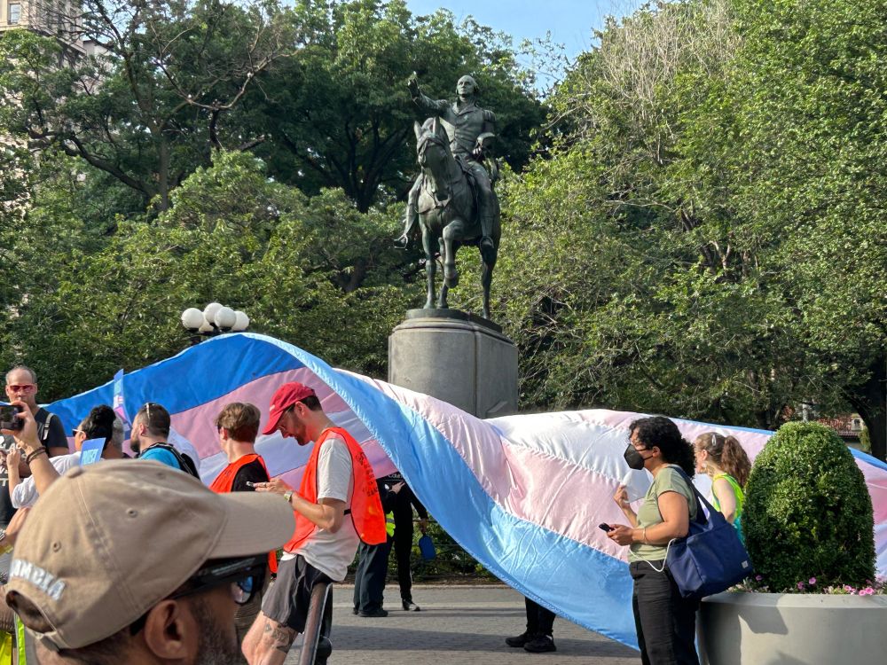 Trans rights demonstration in Union Square with Trans Pride flag out in front of Washington statue.