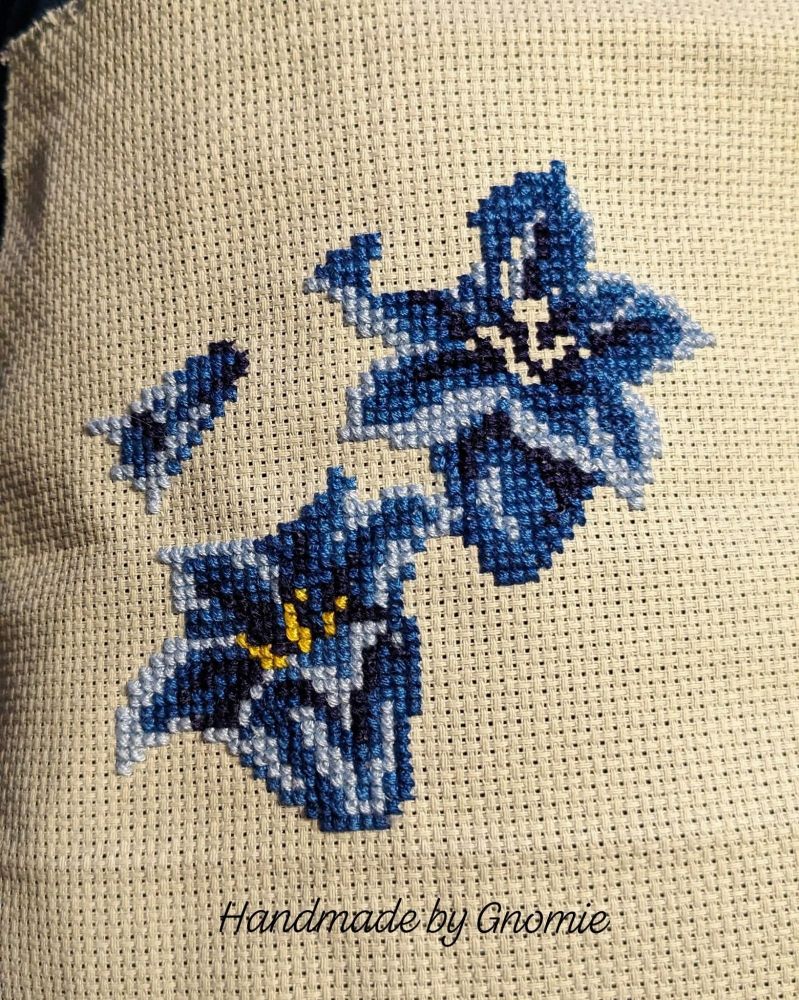 Cross stitch work in progress. Three detailed blue flowers (bluebells?) on pale green Aida cloth. 