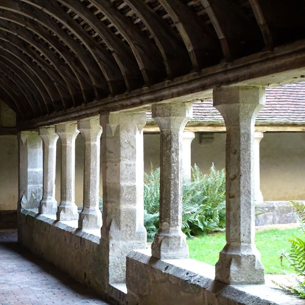 The 16th century cloister of the Convent of St Francis and St Claire. The cloister has simple stone columns and oak beams and looks out into a grassy central area.