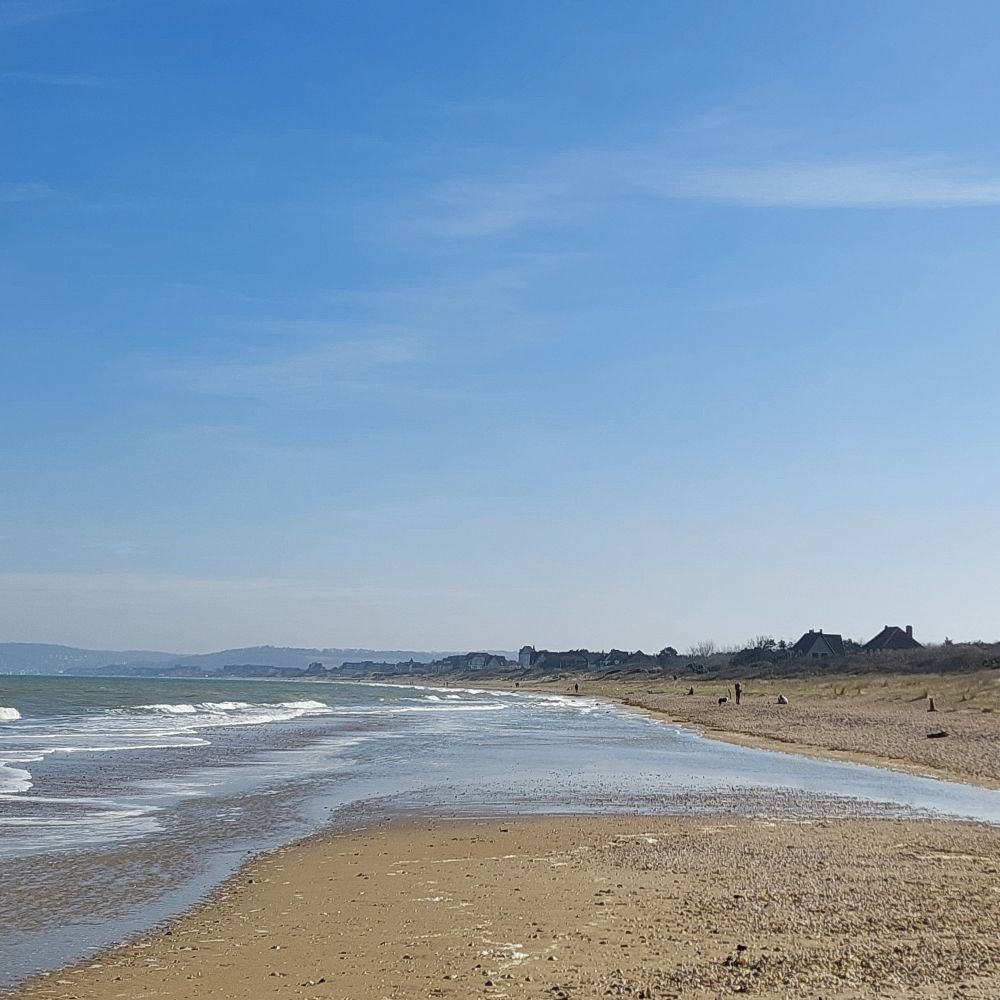A sandy beach with small waves coming in from the left, under a blue sky. 