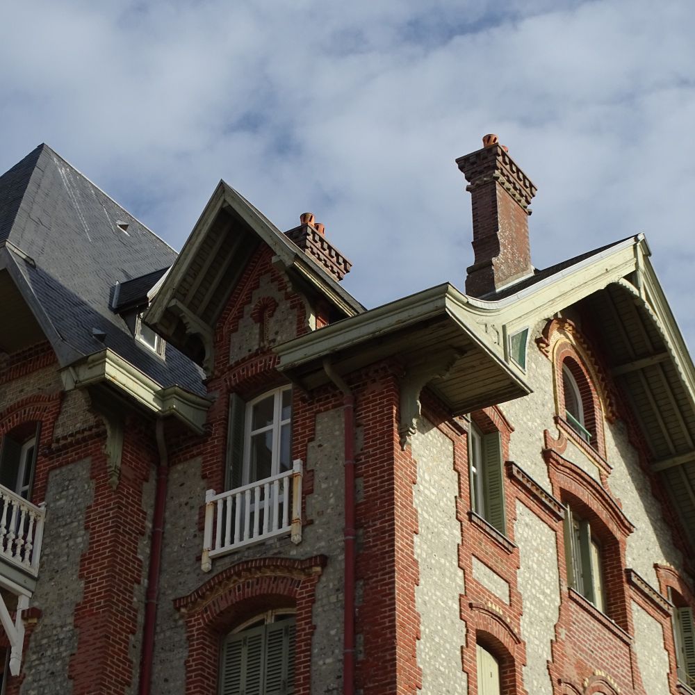 A cropped image of a decorative brick house with many eaves, windows and chimneys