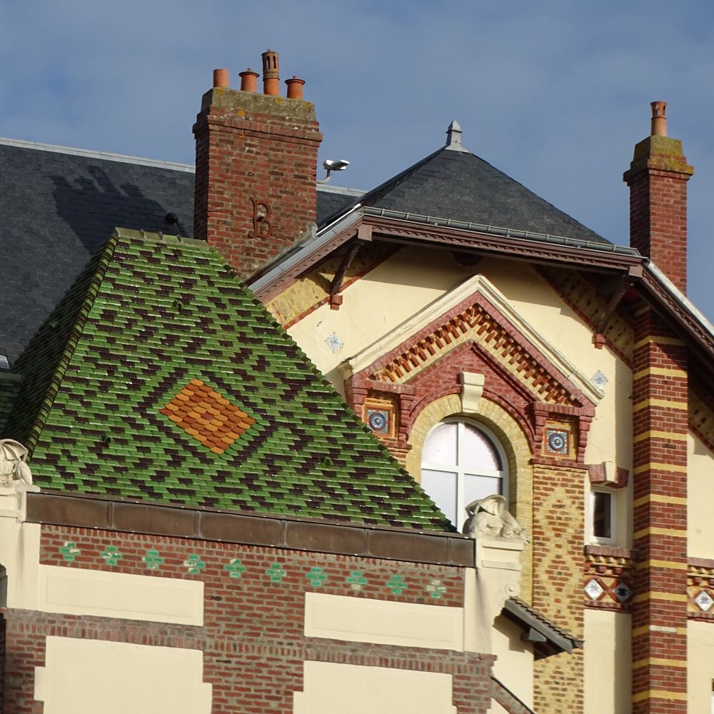 Cropped image of a decorative brick house, with colour patterns in the brickwork and green, yellow and orange glazed tiles on part of the roof