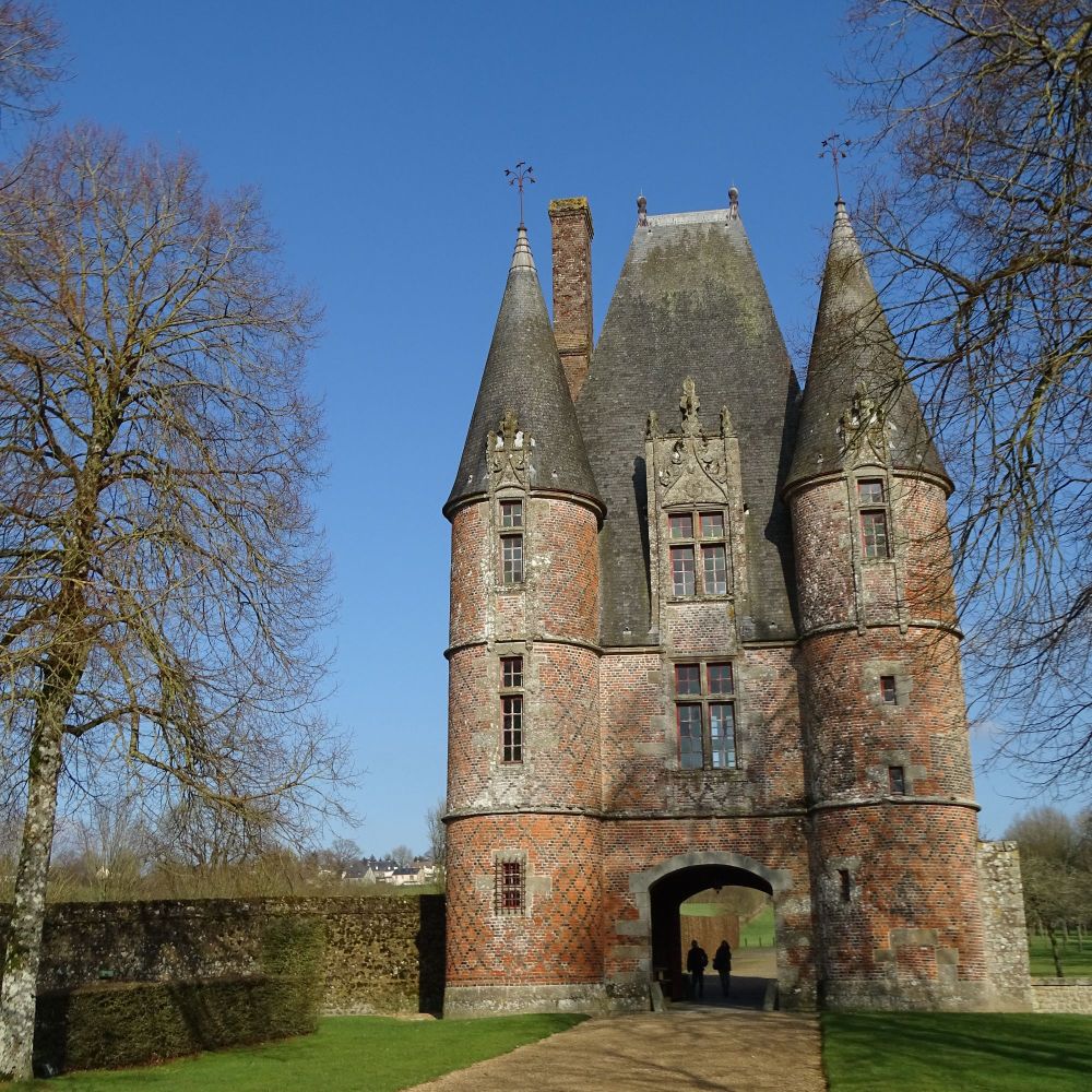 A red-brick gatehouse with three floors of windows, a steep slate roof and conical towers on each corner of the building.
