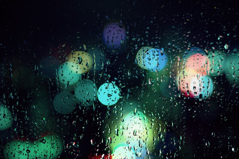 Coloured bokeh orbs of light with greens and teals and a detailed photo of raindrops on glass.