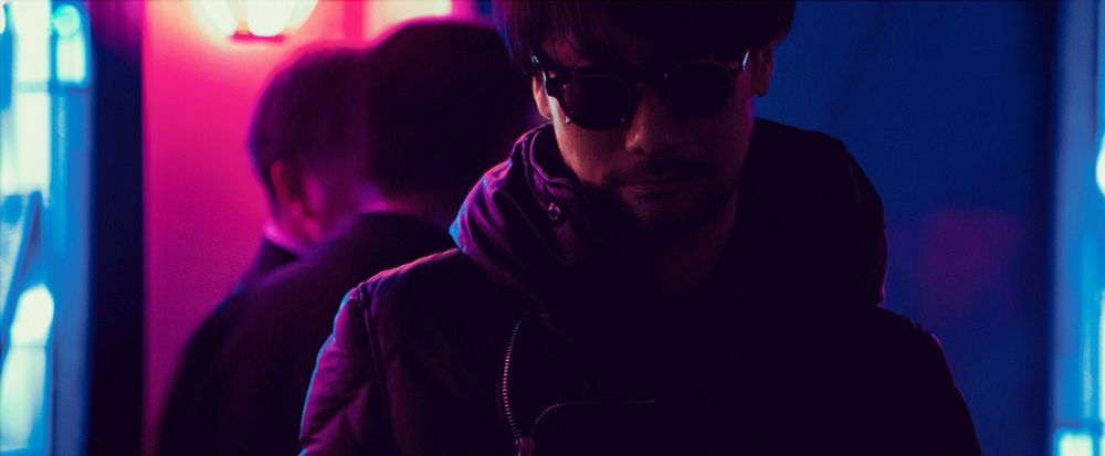 Close-up of Hideo Kojima at night, wearing sunglasses. 