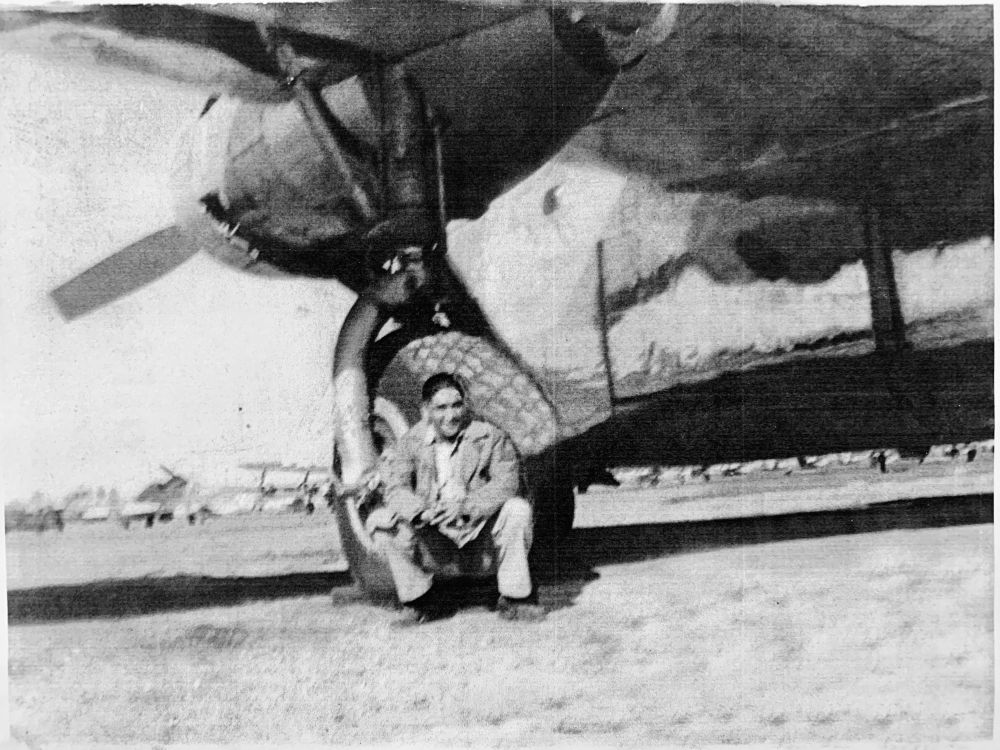 Photo of Joe Yatsattie kneeling in front of the wheel of a WW2 bomber plane.