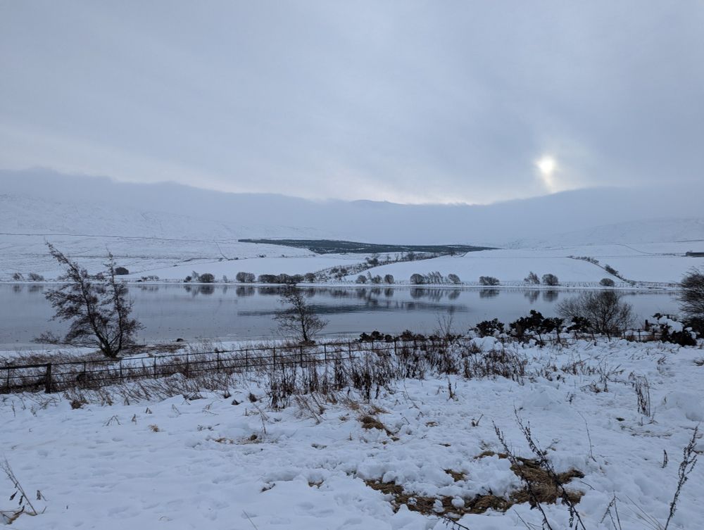 A frozen reservoir surrounded by snowy fields and hills.